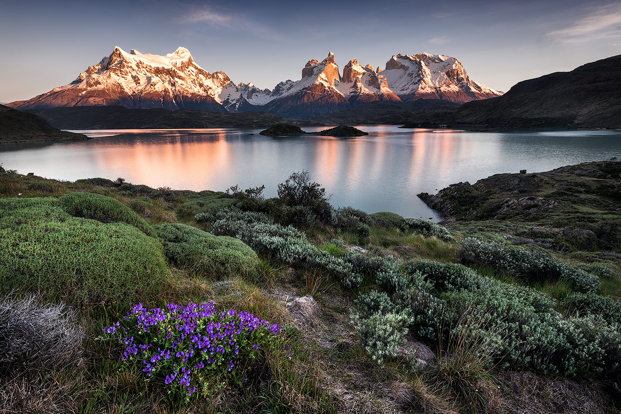 Montanhas nevadas iluminadas pelo sol, lago e vegetação na Patagônia.